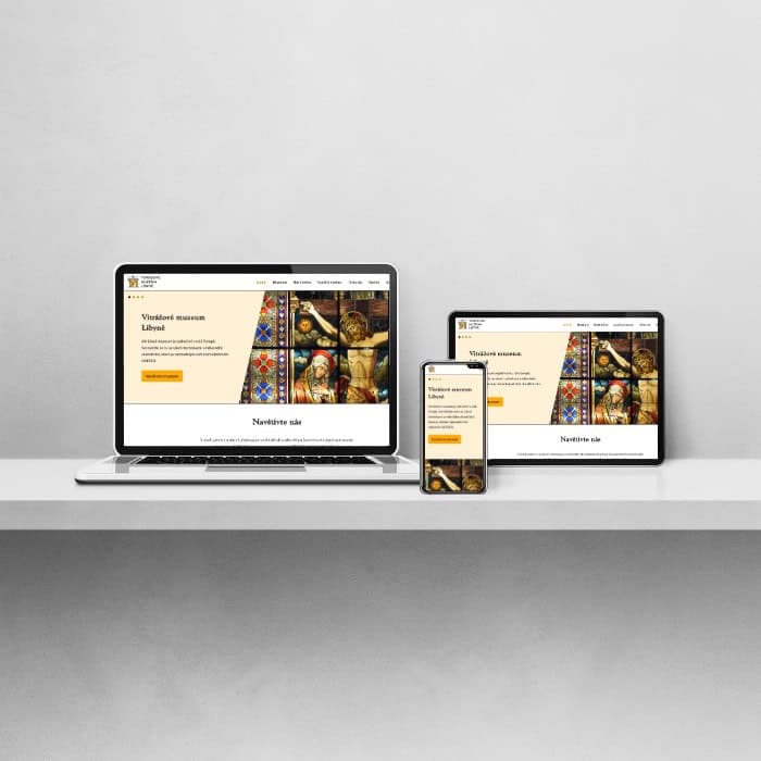 Electronic devices including laptop, tablet, and phone neatly arranged on a table, each showing the homepage of the stained glass museum website.