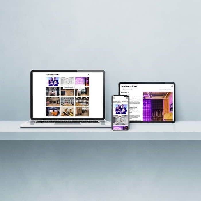 Electronic devices including laptop, tablet, and phone neatly arranged on a table, each showing the homepage of the holub architekti website.
